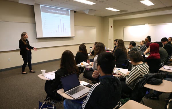 This is an image from TA Orientation, it shows a speaker at the front of the room presenting to a group of seated students