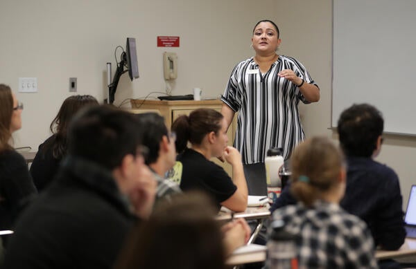 A presenter at TA Orientation stands in front of a classroom of seated grad students