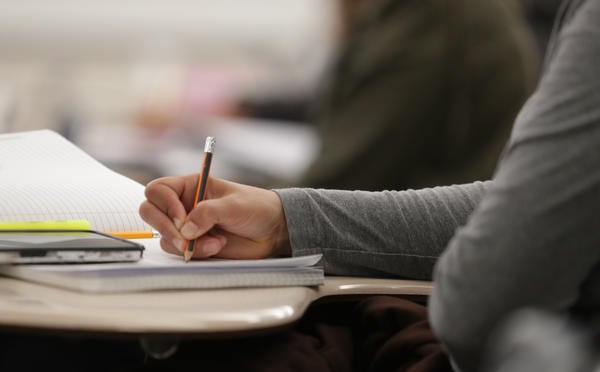 This is an image from TA Orientation, it is a closeup image of a student's hand holding a pen, writing in a notebook